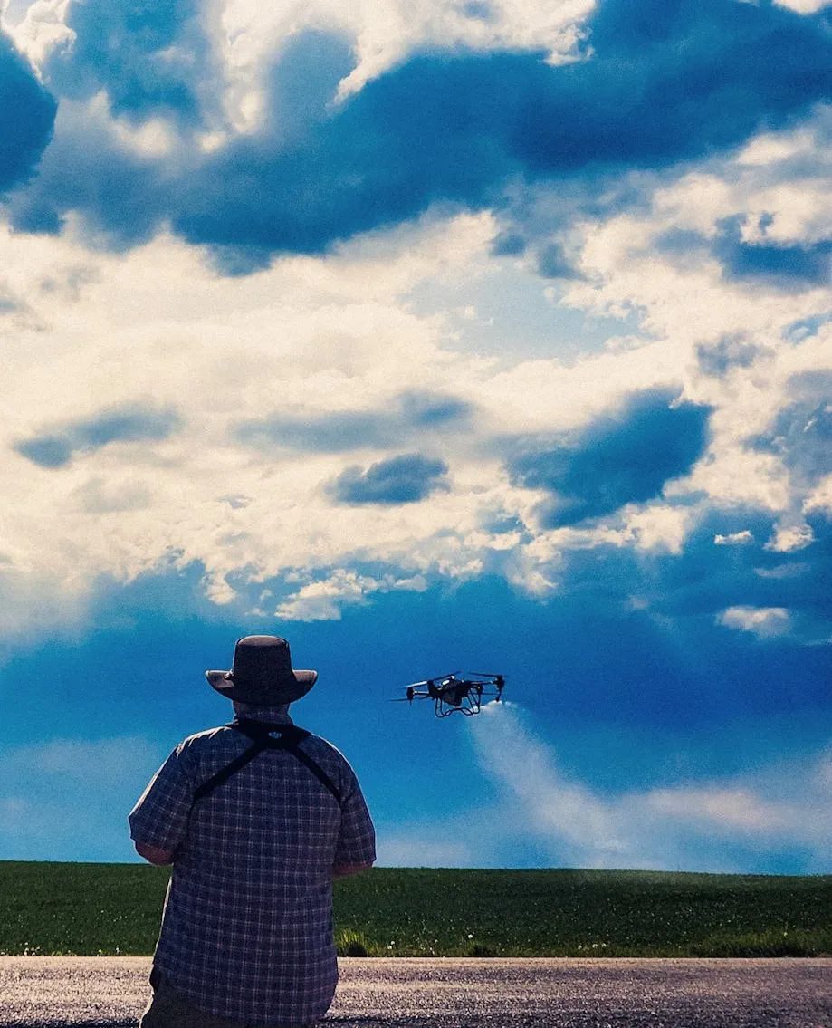 The back of a man who is piloting an agricultural drone that's spraying a field